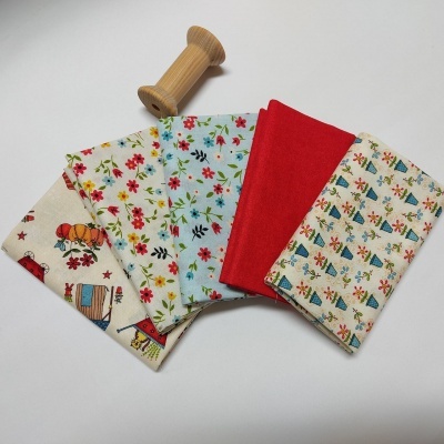 Cinco tecidos estampados com padrões florais e infantis e um carretel de madeira numa superfície branca