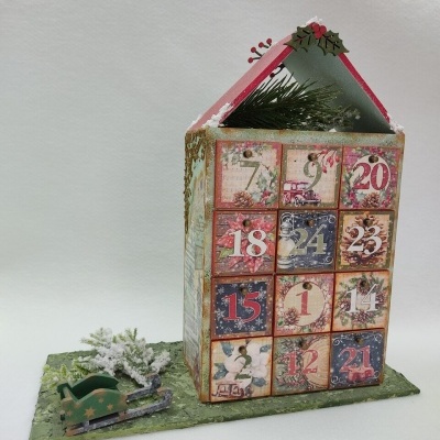 Calendário do advento em forma de casa com gavetas numeradas e trenó verde com árvore