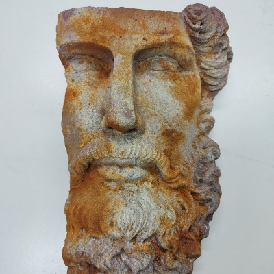 Máscara decorativa cerâmica de rosto masculino com barba e cabelo ondulados em tons castanhos e cinzentos