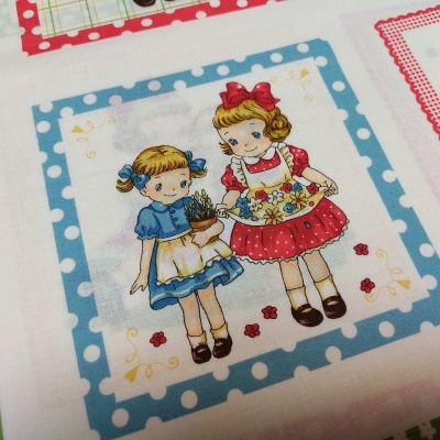 Tecido com desenho de duas meninas em estilo vintage, emolduradas por padrão azul de bolinhas.