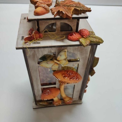 Lanterna decorativa em madeira com detalhes de cogumelos, folhas e frutos coloridos em relevo.