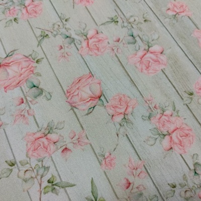 Tecido branco com padrão de rosas cor-de-rosa e folhas verdes sobre padrão de madeira branca