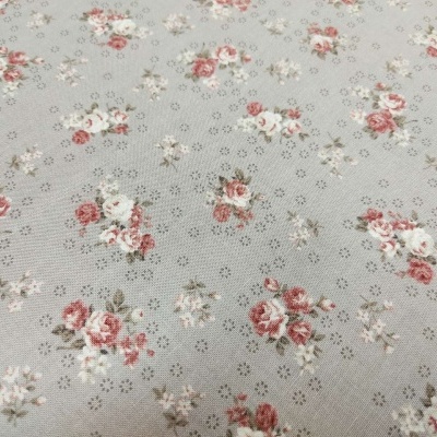 Tecido cinza claro com padrão floral rosa e branco e pequenos círculos perfurados.