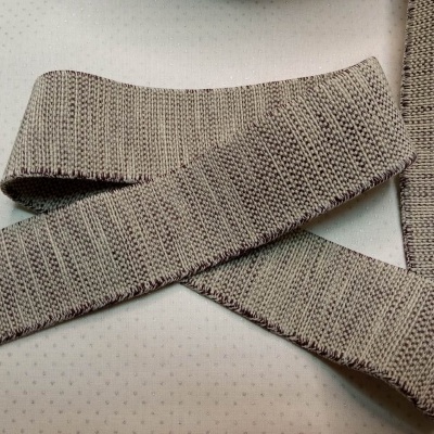 Fita de tecido trançado bege claro com padrão detalhado sobre fundo branco pontilhado.