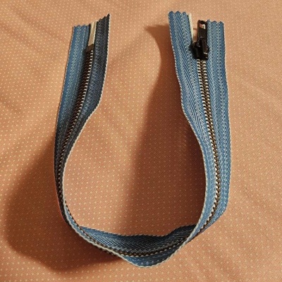 Fecho éclair azul com dentes metálicos sobre tecido bege com pontos brancos