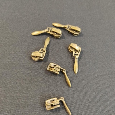 Seis cursores de fecho éclair metálicos dourados sobre fundo cinzento.