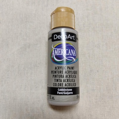 Frasco de tinta acrílica Americana cor Cobblestone com tampa dourada sobre tecido bege