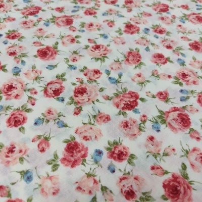 Tecido branco com padrão floral de rosas cor-de-rosa, vermelhas e pequenas flores azuis