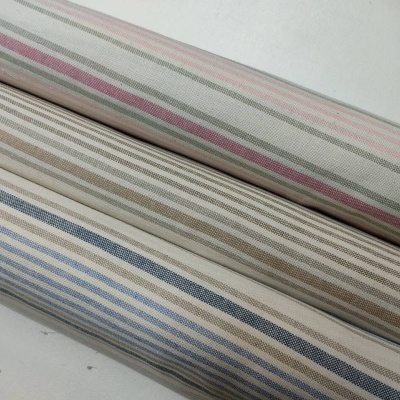 Rolos de tecido listrado em rosa, bege e azul sobre superfície branca