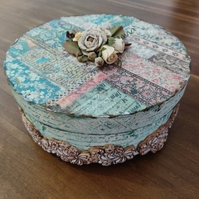 Caixa redonda decorativa com padrões florais e flores artificiais no topo