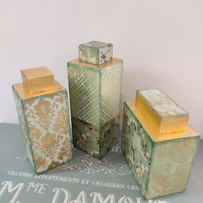 Três caixas decorativas verdes com tampas douradas e padrões florais