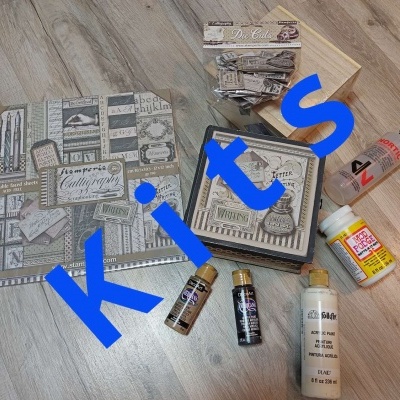 Conjunto de materiais para artesanato com papéis decorativos vintage, tintas acrílicas, cola e verniz sobre mesa de madeira clara.