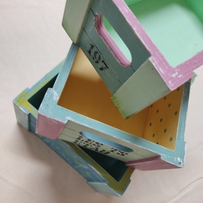 Três caixas de madeira decorativas empilhadas e coloridas em tons pastel com texto e pontos.