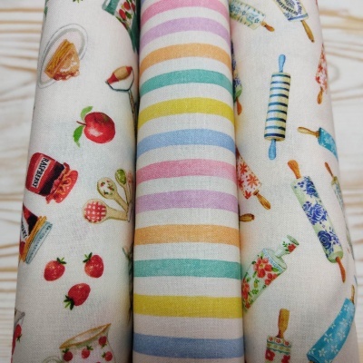 Três rolos coloridos de tecido com padrões variados colocados sobre mesa clara.