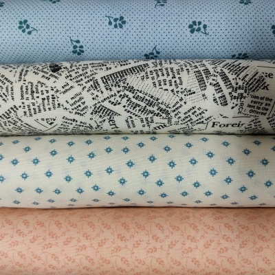 Quatro rolos de tecido empilhados com padrões florais e de texto