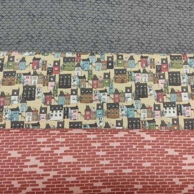 Três tecidos diferentes empilhados com padrões distintos: escamas, casinhas coloridas e tijolos vermelhos.