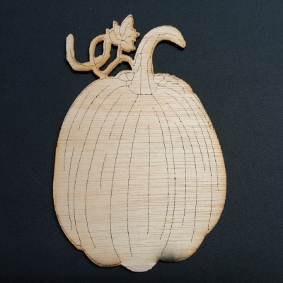Abóbora recortada em madeira clara com linhas gravadas sobre fundo preto