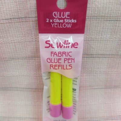Dois recarregadores de cola para tecido amarela da marca Sewline numa embalagem plástica com fundo cor de rosa e vermelho.