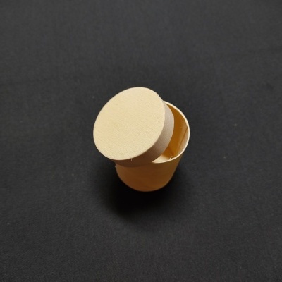 Caixa pequena redonda de cartão amarelo com tampa creme aberta sobre fundo preto