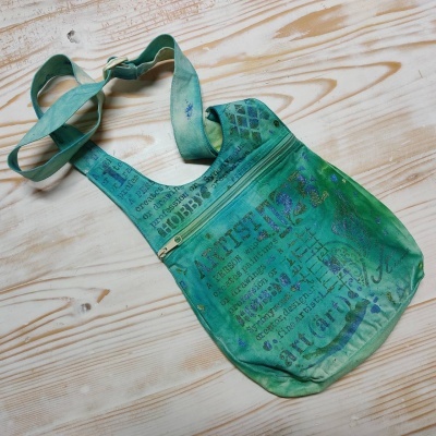 Mala de ombro azul verde com padrão de texto impresso em várias línguas sobre madeira clara