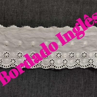 Tecido branco bordado inglês com padrão floral sobre fundo escuro