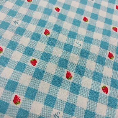 Tecido azul e branco às quadrículas com morangos vermelhos e letras sobre superfície plana