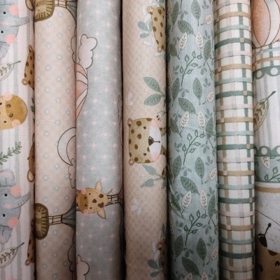 tecidos infantis com padrões de animais e folhas em tons pastel