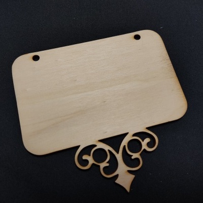 Placa de madeira clara retangular com desenho ornamental cortado a laser sobre fundo escuro
