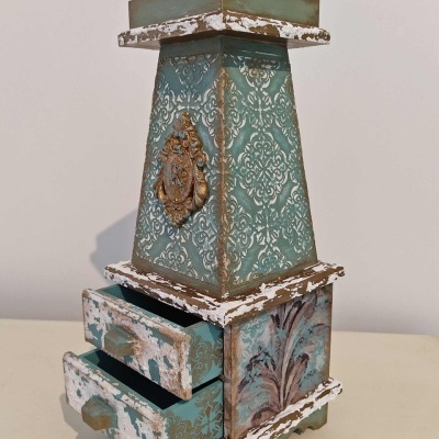 Móvel decorativo pequeno azul e branco com gavetas abertas e ornamento metálico