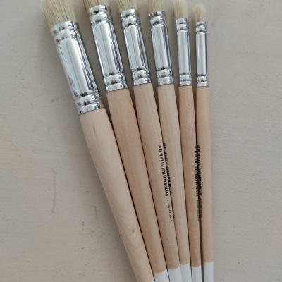 Seis pincéis de pintura de madeira com cerdas brancas em fundo bege claro