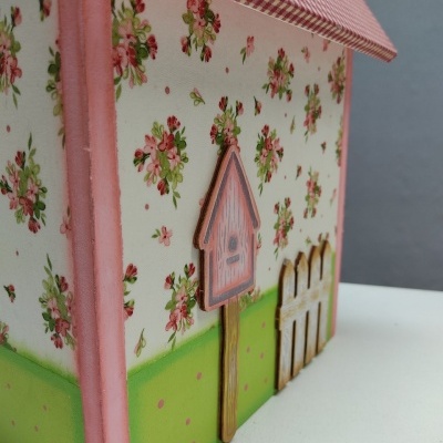 Caixa decorativa em forma de casa com padrão floral, verde, rosa e detalhe em madeira