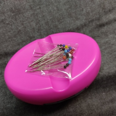 Agulhas com cabeças coloridas sobre caixa oval cor-de-rosa