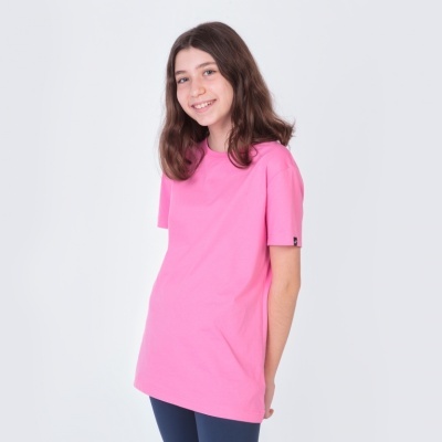 Jovem a sorrir com t-shirt rosa e calças azul-escuras diante de fundo branco