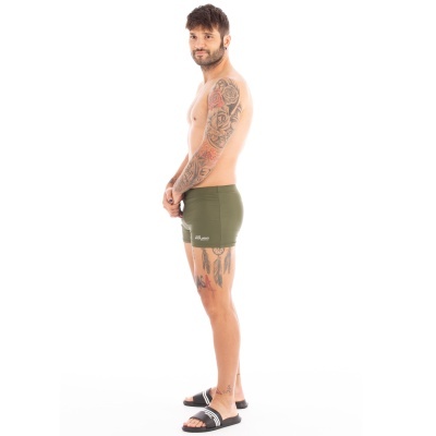 Homem de lado com calções de banho verde-oliva e chinelos pretos