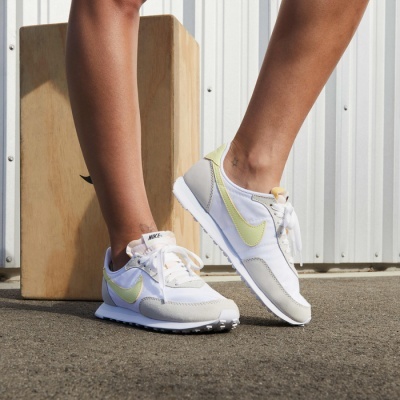 Ténis desportivos Nike brancos com detalhes amarelo pálido e cinza usados em ambiente exterior