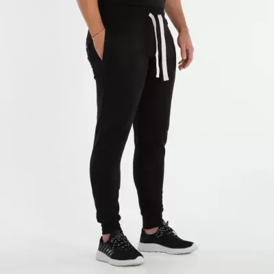 Calças pretas de treino com cordão branco, ajustadas nos tornozelos, usadas com ténis pretos e brancos