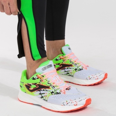 Ténis desportivos branco com verde fluorescente e detalhes coloridos, usados com calças pretas com risca verde.