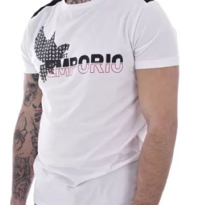 Homem com t-shirt branca e detalhes pretos, com estampa EMPORIO no peito, e tatuagens nos braços e pescoço