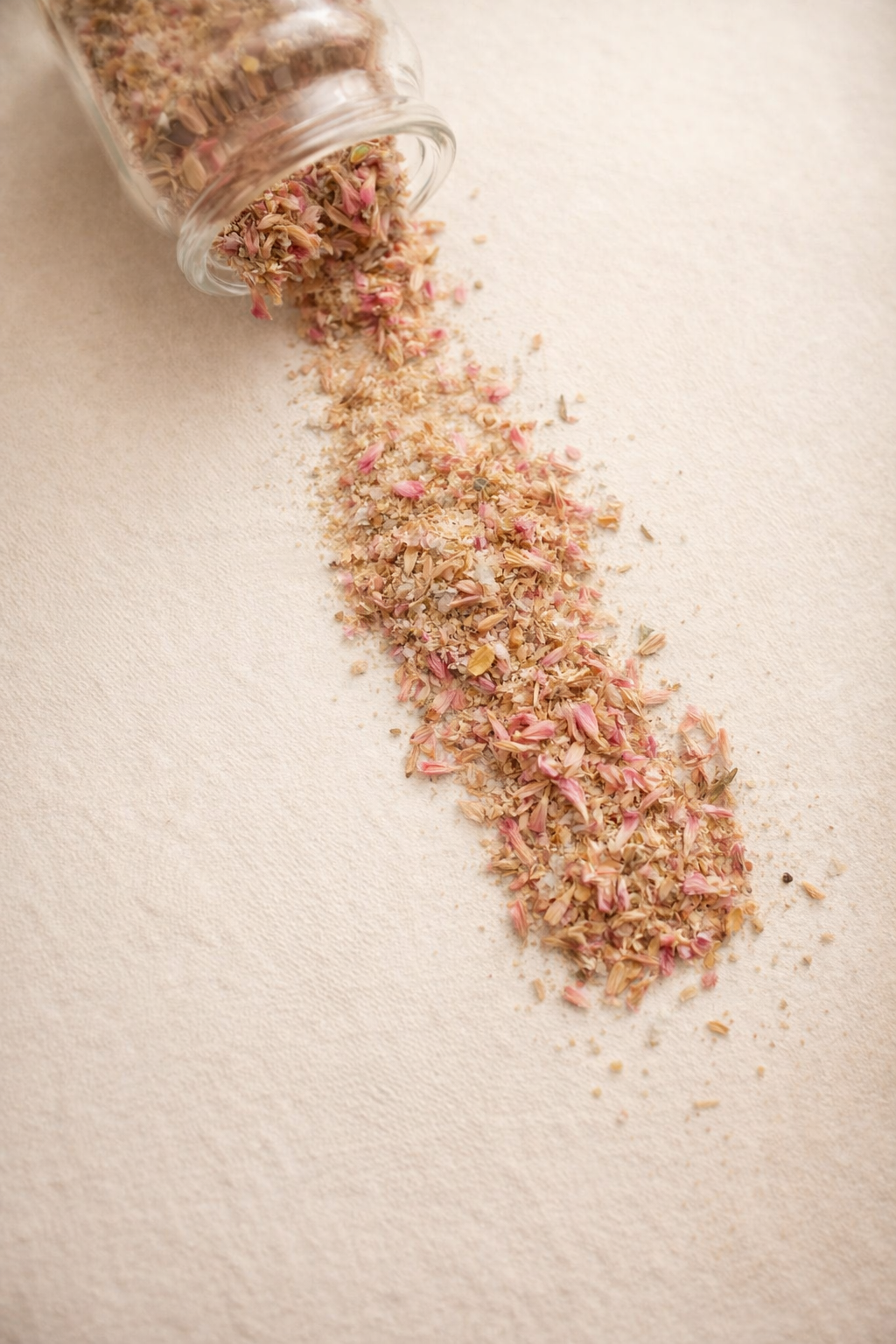 Sais para Duche & Banho - CONFORTO Frasco de vidro deitado com mistura de sal grosso e flores secas rosas e bege espalhadas no chão