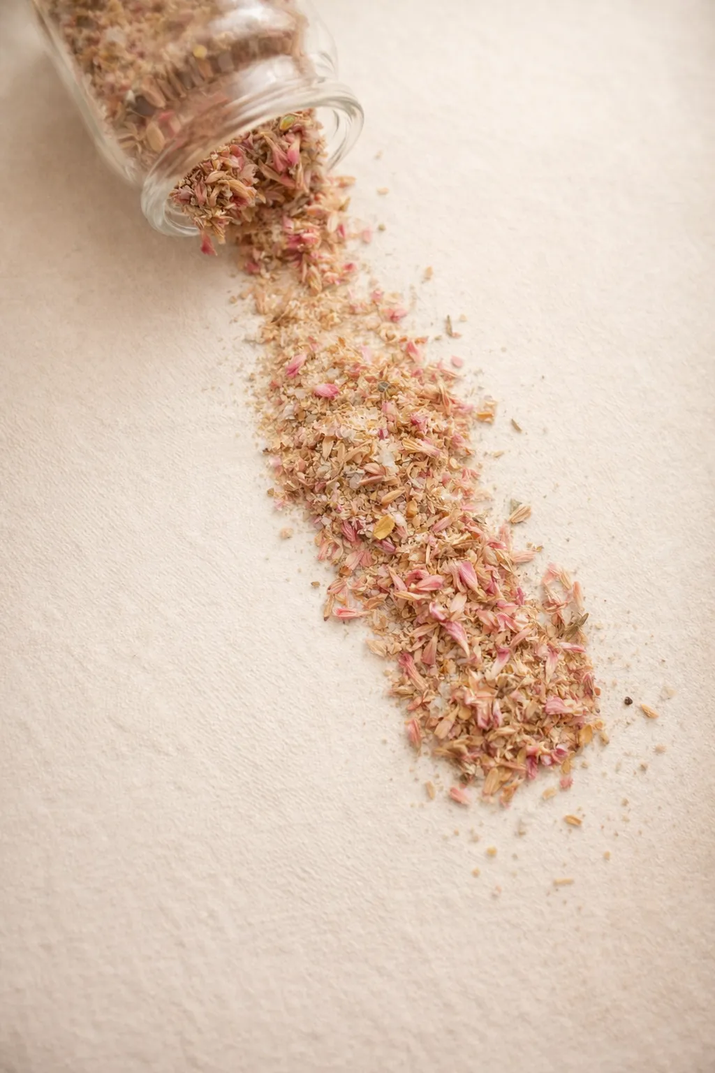 Sais para Duche & Banho - CONFORTO Sais de banho Conforto e ervas aromáticas espalhados a partir de frasco tombado em superfície clara