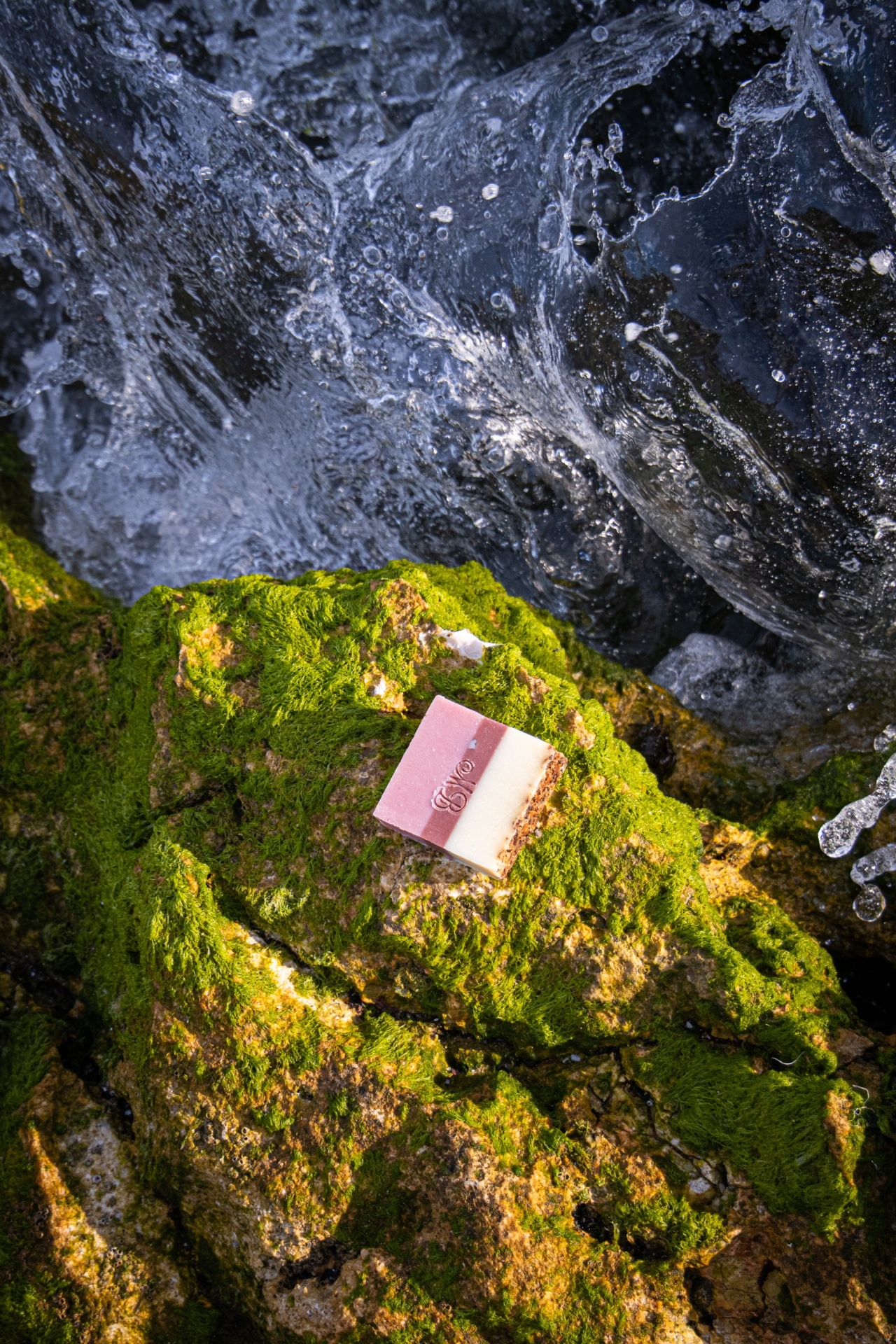 Sabonete natural - PAIXÃO Sabonete bicolor rosa e branco sobre rocha com musgo verde e água ao fundo