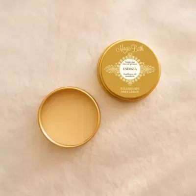 Pote dourado aberto com bálsamo de tangerina Energia ao lado da tampa amarela, tecido claro