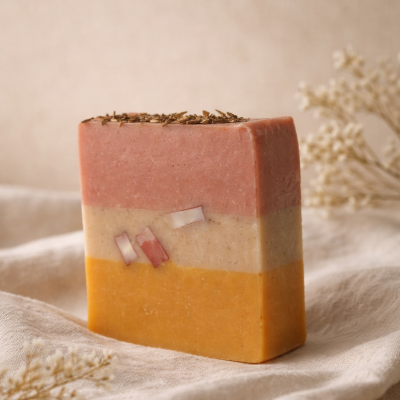 Sabonete artesanal em camadas rosa, bege e amarelo com folhas secas no topo