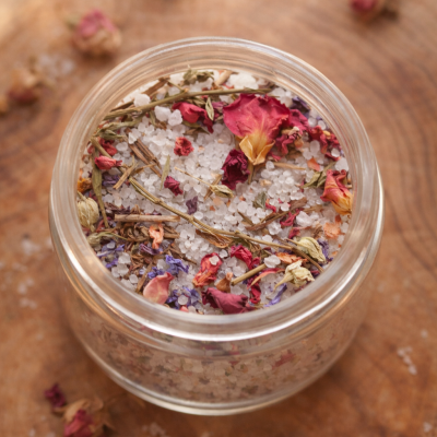 Frasco de vidro com sais de banho e pétalas secas sobre madeira