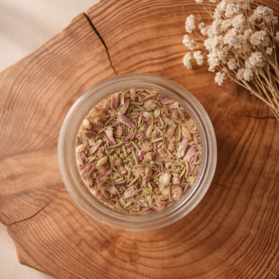 Frasco com mistura seca de flores e ervas sobre tábua de madeira com flores secas ao lado