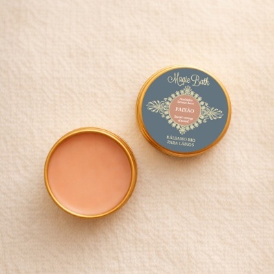 Dois bálsamos labiais em embalagem metálica dourada, um com tampa azul cinza com texto e outro aberto mostrando o produto