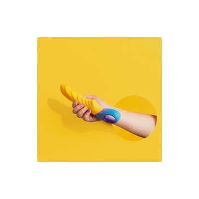 Objeto amarelo com base azul e rosa na mão contra fundo amarelo