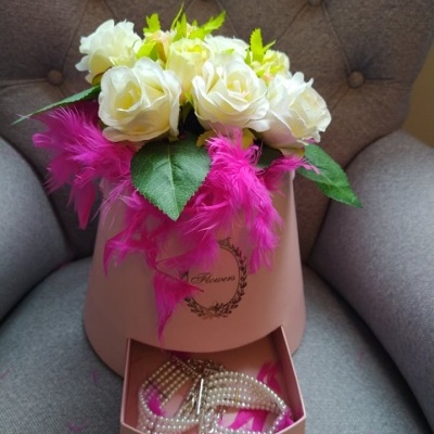 Vaso cor-de-rosa com flores artificiais brancas e penas rosa, com gaveta aberta e pulseiras, numa cadeira cinzenta