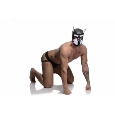 Homem de joelhos com máscara de cachorro preta e branca e roupa interior preta em fundo branco.