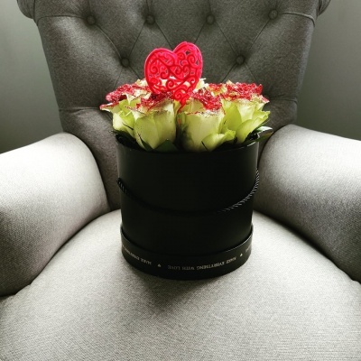 Arranjo de rosas brancas com pontas vermelhas em vaso preto numa cadeira cinza